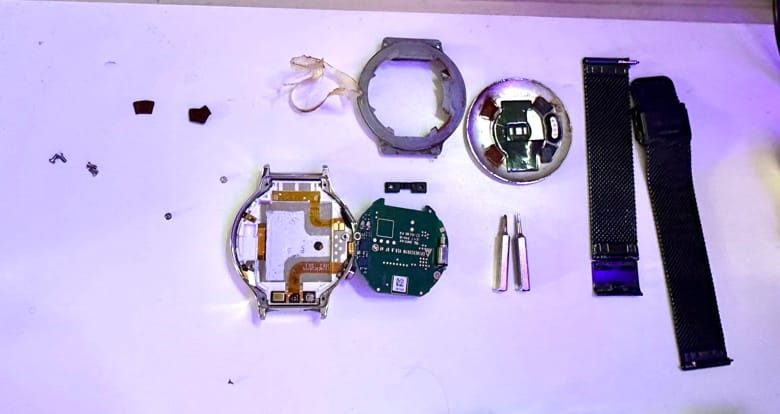 A disassambled Huawei W1 watch, showing various components and screw bits visible, as well as a black metal strap