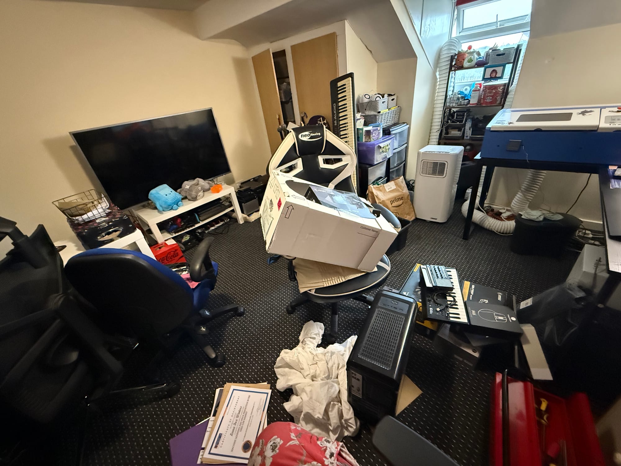 A very messy office, equipment and boxes are strewn all over. A large laser cutter sits in one corner