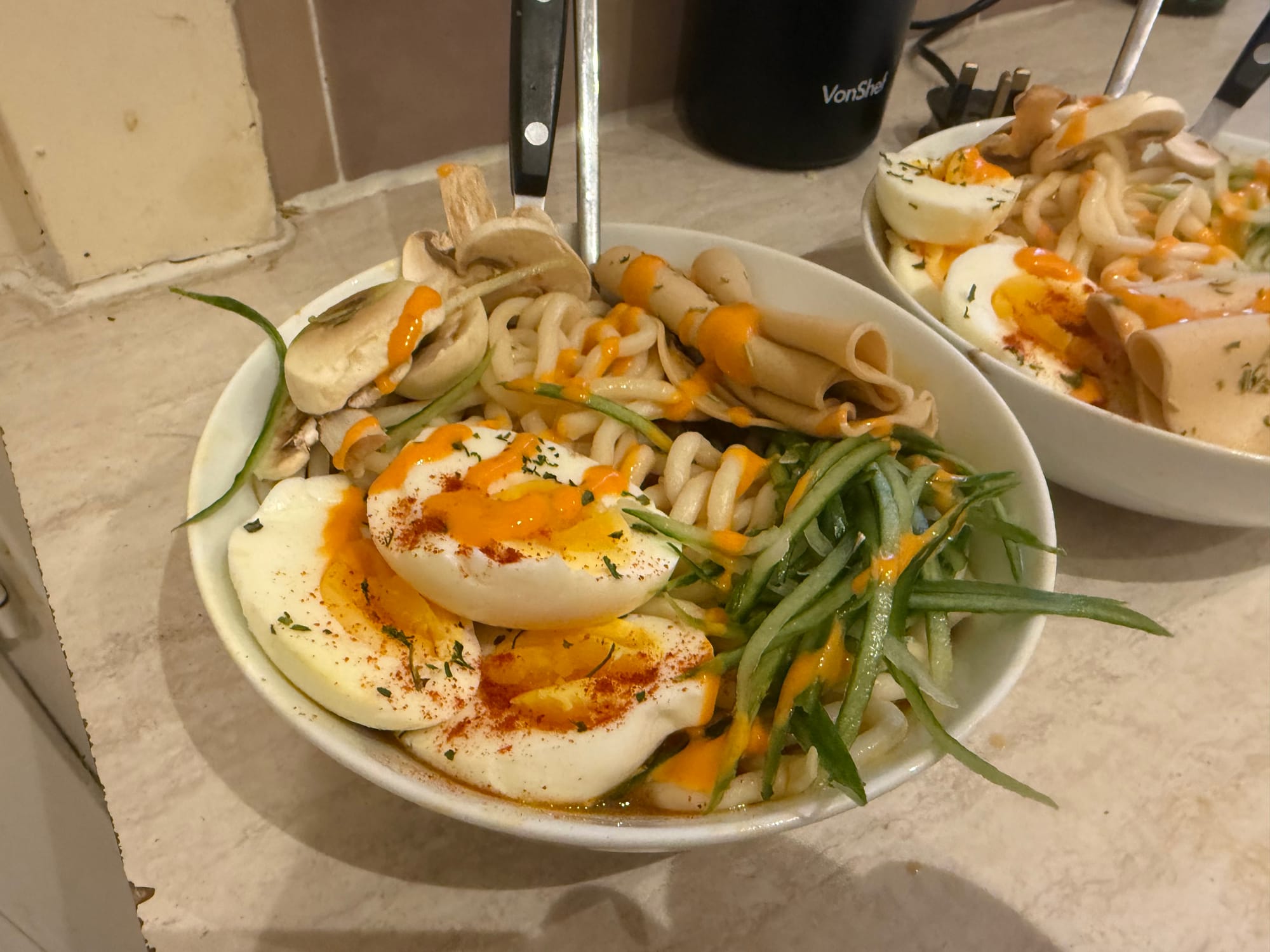 A bowl of ramen noodles, eggs, fresh vegetables and ham