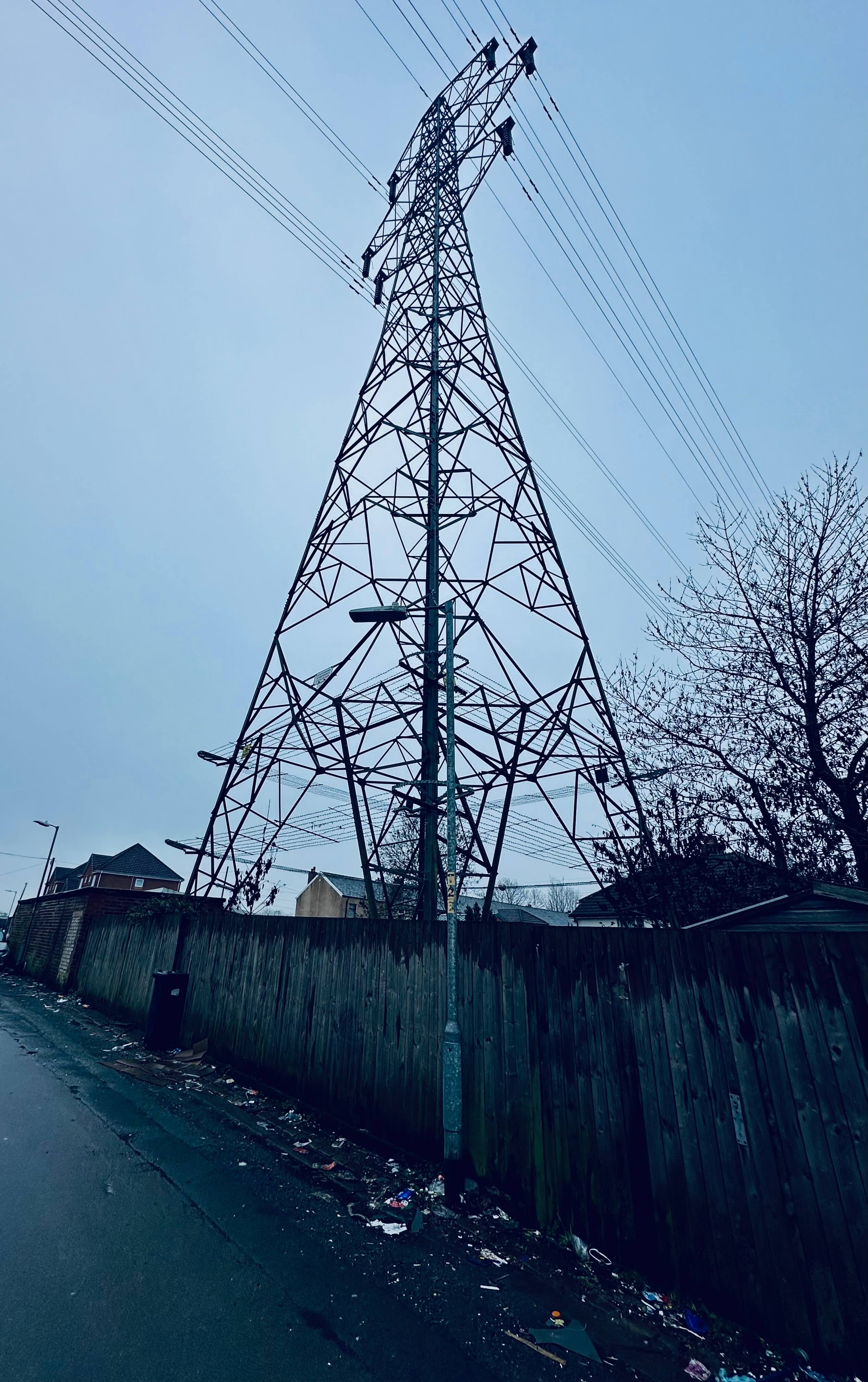 A very desaturated image of an english back street, an electricity pylon dominates a grey sky.